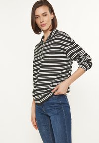 Pullover a righe bianche e nere con zip frontale, texture a coste e maniche lunghe, abbinato a jeans blu.