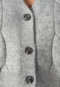 Gray knitted cardigan with a V-neck, featuring four black buttons down the front and ribbed accents at the hem and cuffs.