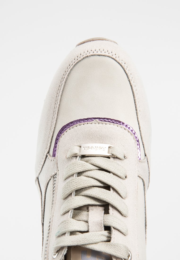 Sneaker beige in suede con colletto imbottito, lacci piatti e un accento viola attorno al battistrada. Presenta una placca logo argentata sulla linguetta.