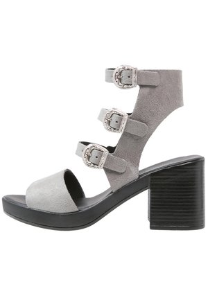 Sandales à talons hauts en daim gris avec trois sangles ajustables à boucle et un large talon bloc noir. Semelle intérieure lisse avec un design à bout ouvert.