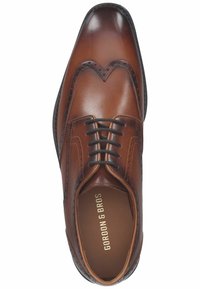Braune Leder-Hausschuhe mit Flügelspitze, runder Zehenform, durchbrochene Details, schwarze Schnürsenkel und strukturiertem Sohlen.