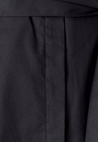 Tessuto nero con una superficie liscia, caratterizzato da pieghe verticali e una cucitura dritta. Design semplice, senza hardware o dettagli visibili.