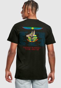 Svart bomulls t-skjorte med en fargerik grafisk design på baksiden, som viser et egyptisk inspirert motiv og turnédetaljer med fet skrift.