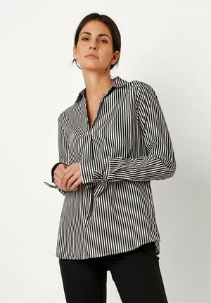Gestreiftes schwarz-weißes Hemd mit langen Ärmeln, Kragen und Bindebanddetail an den Manschetten, präsentiert an einem Modell vor einem neutralen Hintergrund.