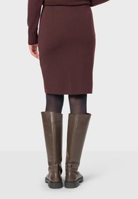 Gonna a matita borgogna con spacco sul retro, abbinata a stivali in pelle marrone al ginocchio. Il materiale sembra morbido con una silhouette aderente e cuciture regolabili.