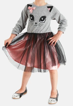 Szara sukienka z długim rękawem z nadrukiem twarzy kota, różową kokardką, warstwową różową satyną i czarną spódnicą z tiulu. Czarne buty z nadrukiem kota.