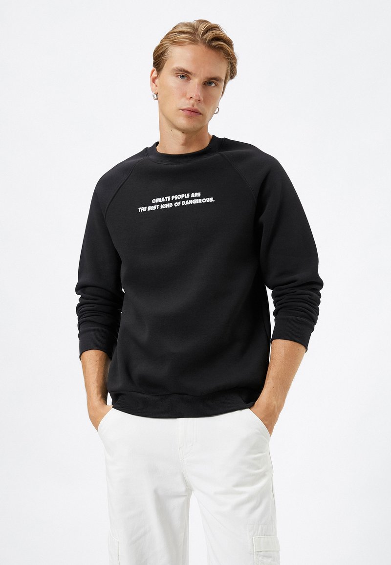 Zwarte sweatshirt met raglanmouwen, geribbelde manchetten en zoom. Heeft witte tekst met de boodschap: "Geweldige mensen zijn de beste soort gevaarlijk."