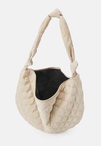 Borsa a tracolla beige trapuntata con una morbida tracolla intrecciata. Presenta una parte superiore aperta e un interno nero, con una superficie testurizzata e dettagli di cucitura.