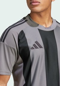 Siva atletska majica s crnim vertikalnim prugama, okruglim ovratnikom i Adidas logom u tamnosivoj boji, izrađena od lagane, teksturirane tkanine.