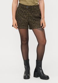 Leopard print shorts in olive green fabric, featuring a button closure, paired with sheer black tights and chunky black ankle boots.