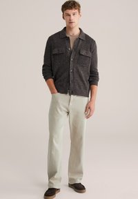 Grå ullkofta med knäppning och två bröstfickor, i kombination med ljusgröna byxor och bruna skor. Enkel, funktionell design.