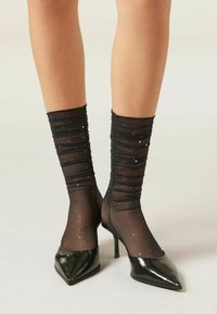 Calzini neri con arricciature e accenti a pois argentati, realizzati in materiale leggero, abbinati a décolleté nere in vernice a punta.