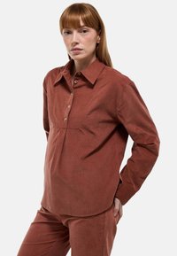 Chemise en velours côtelé marron à boutons avec col, dotée d'une patte de boutonnage à l'avant, de manches longues et d'une silhouette décontractée. Texture douce et coutures discrètes.