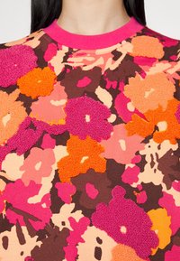 Blommönstrad sweatshirt i livliga orange, rosa och bruna färger, med en texturerad yta och en rosa ribbad krage.