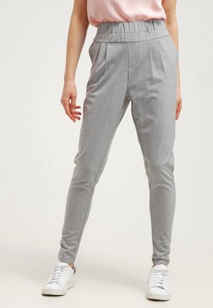 Graue, enganliegende Hose mit hohem elastischem Bund, ausgestattet mit vorderem Faltenwurf und glattem Stoff. Getragen mit weißen Sneakers.