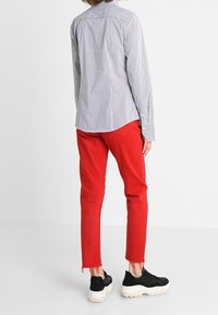 Camisa de manga larga a rayas en tonos azules y blancos, combinada con pantalones cortos rojos con dobladillos deshilachados y zapatillas de plataforma negras.