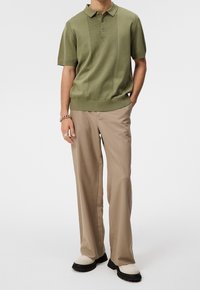 Polo tricoté vert olive avec un devant texturé, assorti à un pantalon beige clair plissé et des chaussures épaisses noires et blanches.