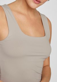 Beige tank top with a square neck design, made from a smooth, stretchable fabric, featuring wide shoulder straps and a fitted silhouette.