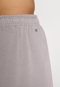 Hallid hallid dressipüksid elastse vöökohtaga, millel on tagasihoidlik külglogo, valmistatud pehmest, tekstuurist kangast. Nähtavaid taskuid ei ole.