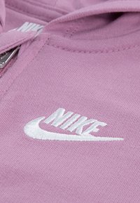 Hanorac roz din bumbac cu logo-ul Nike brodat alb, textură netedă, închidere cu fermoar și glugă rotunjită.