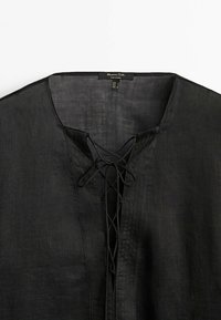 Chemise en lin noire avec col en V et détail lacé croisé au niveau de l'encolure, comportant une petite étiquette intérieure indiquant la taille.