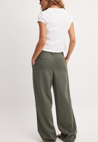 Bela kratka majica s kratkimi rokavi, v kombinaciji z zelenimi visokimi širokimi hlačami, ki imajo stranske žepke in subtilne detajle na zadnjem žepu.