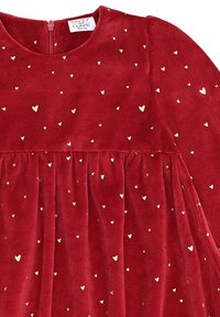 Abito in velluto rosso con scollo rotondo, maniche lunghe e gonna arricciata, decorato con piccoli motivi a forma di cuore dorati.