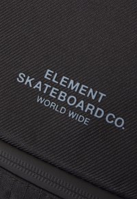 Czarna teksturowana tkanina zawiera słowa "ELEMENT SKATEBOARD CO." oraz "WORLD WIDE" w jasnoniebieskim kolorze, umieszczone w wyraźny sposób na powierzchni.