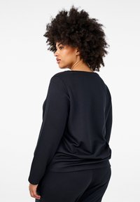 Svart långärmad sweatshirt med avslappnad passform, slät textur och rund halsringning, ihop med matchande mörka byxor.