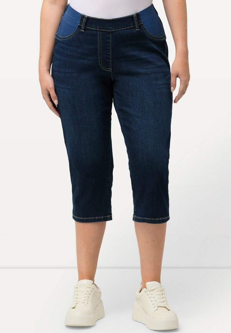 Tummansiniset farkkushortsit, joissa on keskikorkea vyötärö, etutaskut ja ommeltu lahje. Yhdistetty valkoisiin korko-pohjallisiin tennareihin.