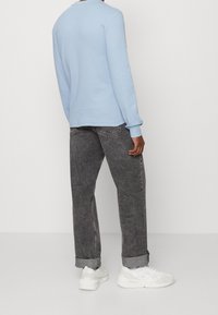 Světlemodrá mikina s dlouhým rukávem a žebrovanou texturou, zkombinovaná s tmavě šedými rovnými džíny, s ohrnutými manžetami a bílými teniskami.