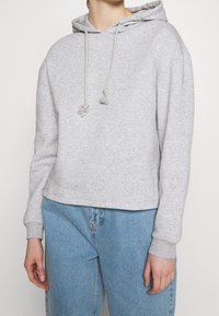 Hoodie grigio corto realizzato in tessuto morbido, con cappuccio con cordini e polsini a costine. Abbinato a jeans chiari a vita alta.