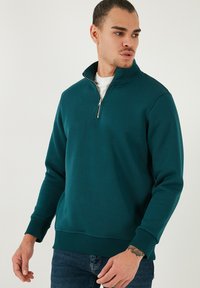 Felpa zip-up color turchese realizzata in materiale morbido, con colletto alto, maniche lunghe e polsini e orlo a coste.