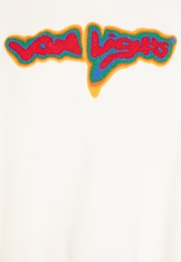 Testo "Low Lights" in rosso con contorno ricamato fuzzy verde, blu e arancione su tessuto bianco.