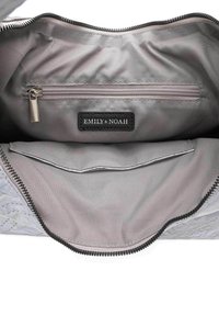 Interior gris de un bolso que presenta un bolsillo con cremallera y una etiqueta negra con "EMILY & NOAH" en relieve. Tela suave con acentos cosidos.