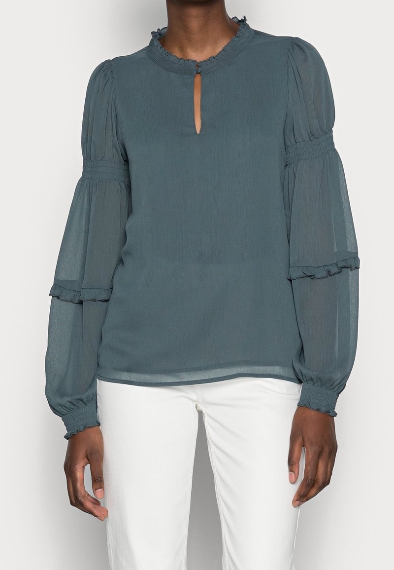 Blouse teal en tissu léger, avec un décolleté en trou de serrure, un ourlet à volants et des manches bouffantes volumineuses avec des poignets froncés.