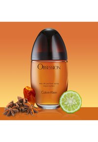 Flacon de parfum Calvin Klein Obsession, en verre ovale avec un liquide ambré, bouchon en dôme noir, accompagné d'anis étoilé, d'ambre et de citron vert.