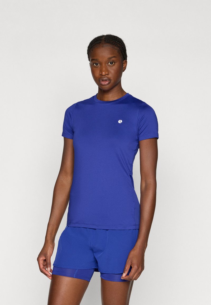 Lila sportpóló rövid ujjal és kerek nyakkivágással, megegyező rövidnadrággal párosítva. A pólón egy kis fehér logó található.