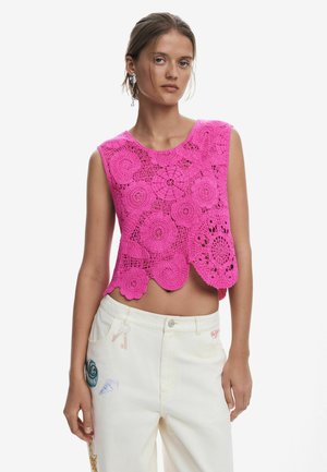 Top court en crochet fuchsia avec des motifs floraux et un ourlet festonné. Assorti à un jean blanc avec des accents brodés colorés.