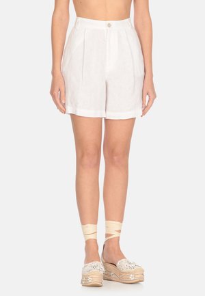 Shorts bianchi in lino con vita alta, pieghe e chiusura con bottone frontale. Abbinati a scarpe espadrillas decorative con accenti floreali.