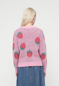 Ροζ πλεκτό πουλόβερ με αφράτη υφή και σχέδια από πράσινες και κόκκινες φράουλες. Λαιμόκοψη και μανσέτες με ριμπ ύφανση. Το τελείωμα φτάνει στη μέση.