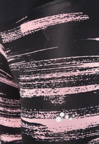 Czarno-różowe legginsy z abstrakcyjnym wzorem pędzla oraz czterema małymi białymi okrągłymi kropkami po prawej dolnej stronie.