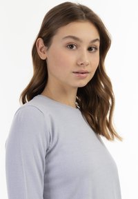 Pulover lung cu maneci lungi, de culoare gri deschis, cu decolteu rotund. Textură moale și siluetă ajustată, cu cusături ribbate la decolteu și umeri.