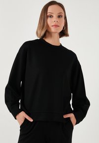 Felpa nera con collo rotondo, maniche lunghe e vestibilità comoda. Realizzata in tessuto morbido con una superficie liscia e polsini a costine.