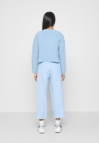 Maglione corto azzurro chiaro con texture e pantaloni abbinati a gamba larga. L'outfit presenta un tessuto morbido e una vestibilità rilassata, abbinati a sneakers.