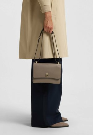 Borsa a tracolla in pelle testurizzata grigia con chiusura a logo dorato, design semplice e tracolla regolabile, tenuta da una persona con un cappotto beige.