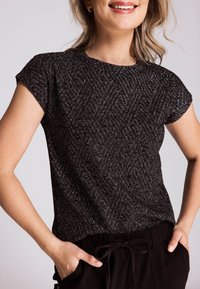 Schwarzes Kurzarmshirt mit strukturierter Musterung, Rundhalsausschnitt und leicht abfallenden Schultern, kombiniert mit schwarzen Jogginghosen mit Kordelzug.