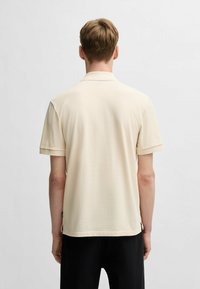 Polo a maniche corte in beige chiaro, realizzato in tessuto morbido, con colletto e sottili spacchi laterali all'orlo.