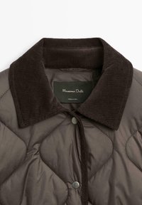 Gequilted bruin pufferjack met een donkere corduroy kraag, drukknopen aan de sluiting en een gestructureerd ruitpatroon op de stof.