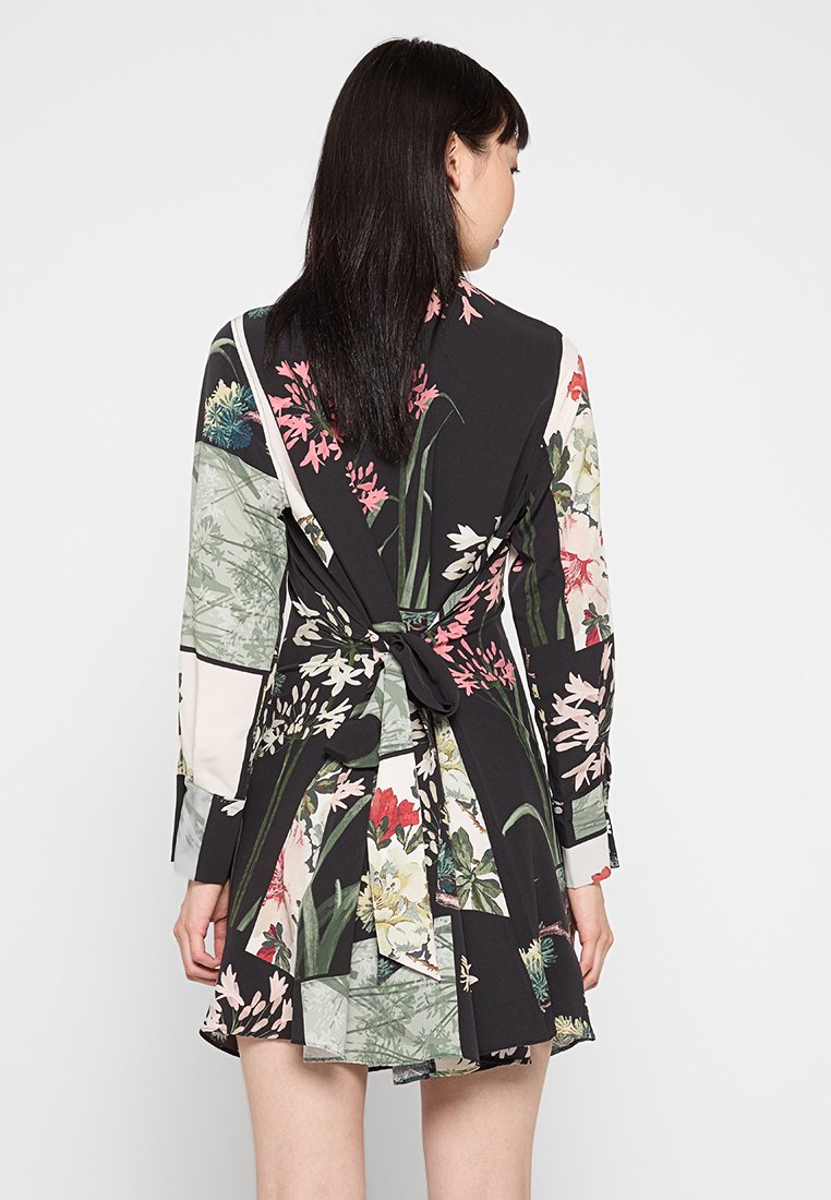 Bloemmotief jurk met een zwarte basis, lange mouwen, strik taille en diverse groene en roze accenten. Kenmerkt een gelaagde rok ontwerp.